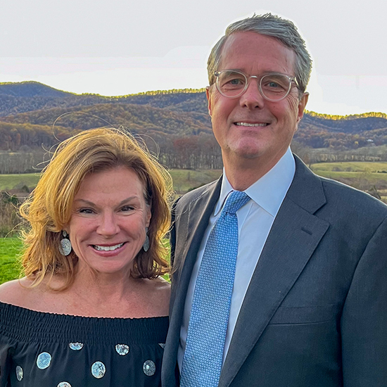 Smiling man and woman outdoors with mountains behind them.