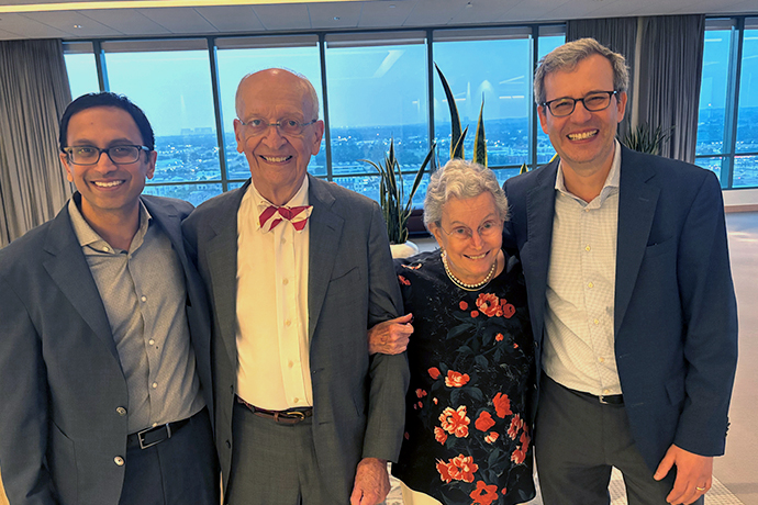 Three men and a woman pose in front of a wall of windows.