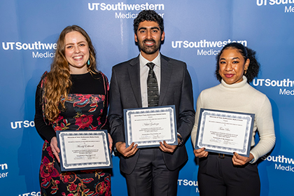 3 people hold award certificates in front of blue UTSW backdrop, from left woman with long brown hair, man with dark curly hair and beard, shorter woman with dark hair in ponytail