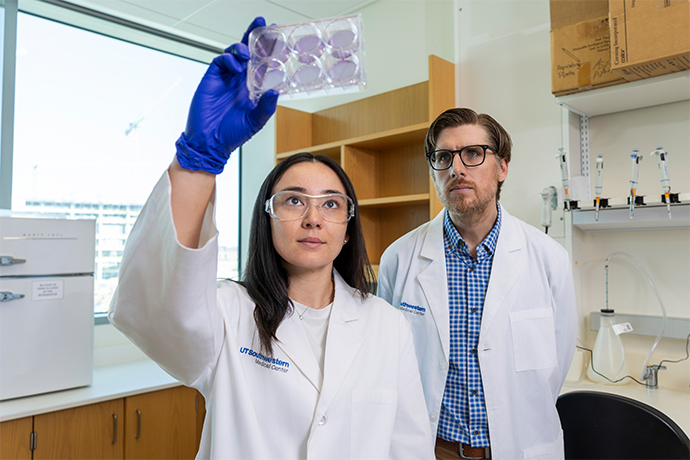 woman with long dark hair and bearded man in glasses, both in white lab coats, look up thru a set of 6 glass slides