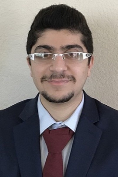 headshot of man with dark hair, glasses and beard in dark suit and tie