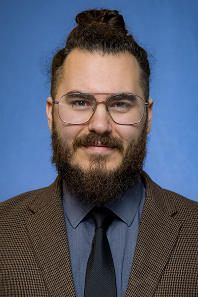 headshot of man with topknot hair, glasses and full dark beard