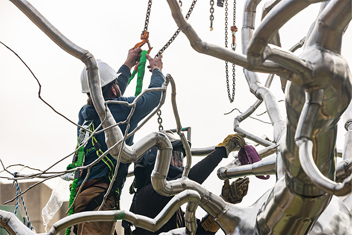 Two workers attaching a work of art to a crane with chains.
