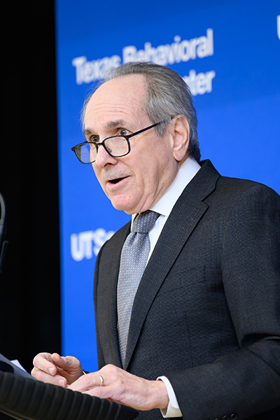 Man wearing suit and glasses speaks from podium.