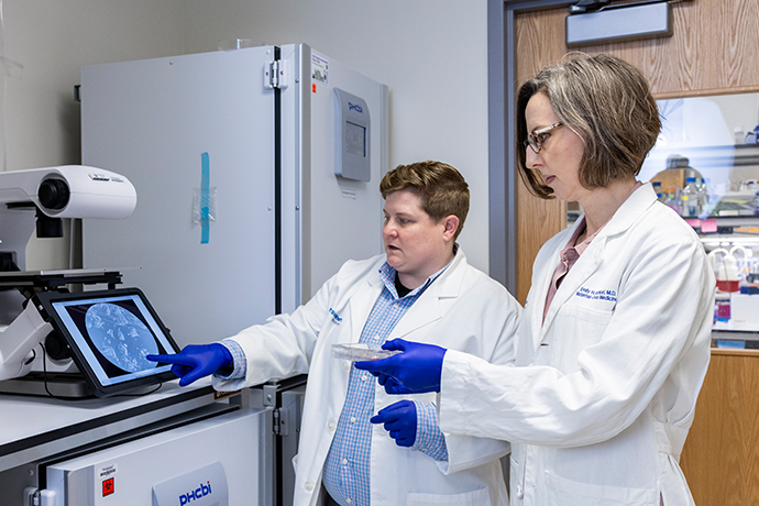 2 doctors in white lab coats and blue gloves discuss image on tablet