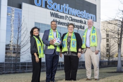 4 people in yellow high-vis yellow scarves holding soccer balls outsite UTSW hospital building