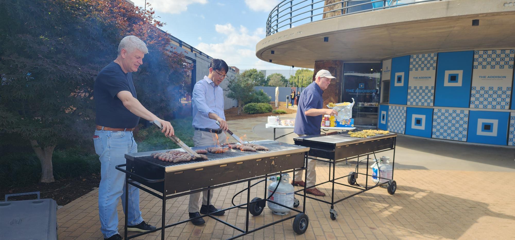 Our Inaugural Chair, Dr. Gaudenz Danuser, one of our faculty, Dr. Jeon Lee, and our Department Administrator, Lance Holmes at barbecue grills against the backdrop of the Addison Performing Arts Center