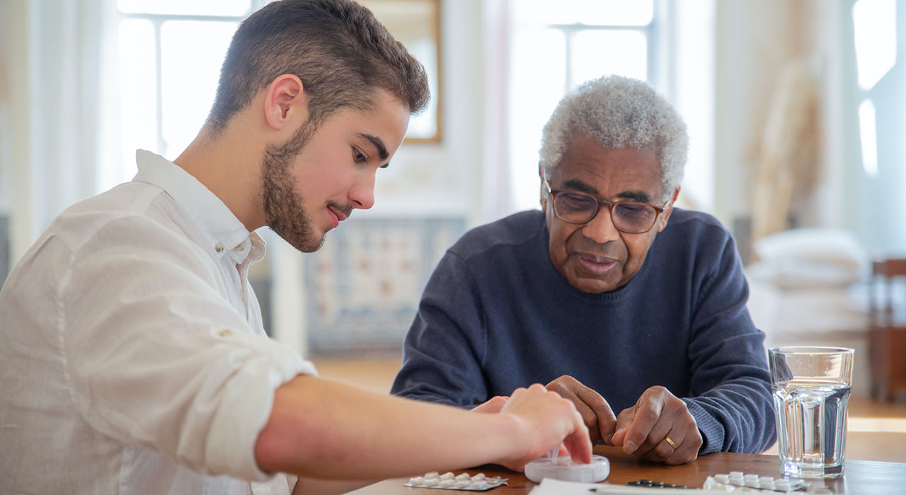 A male student assisting elderly patient with medication