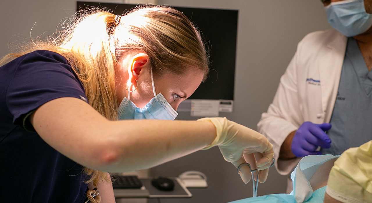 A woman wearing a surgical mask and a look of intense concentration holding a medical tool