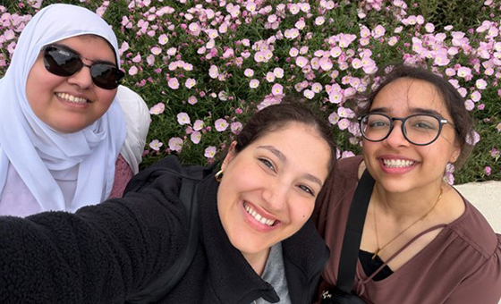 3 women hugging outdoors with flowers in the background