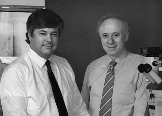 Drs. Brown and Goldstein standing next to a photomicroscope