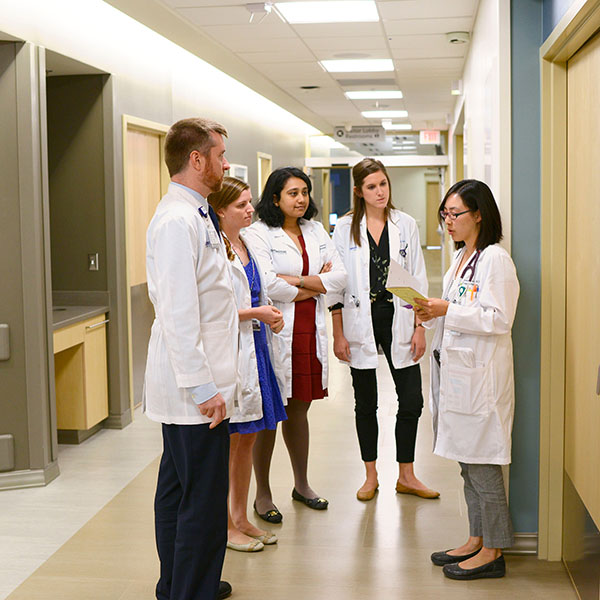 Five doctors standing in a hopsital hallway wearing white coats.