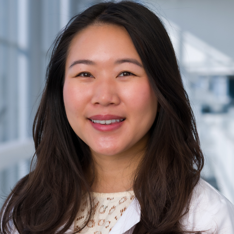 Smiling woman with long black hair wearing white lab coat.