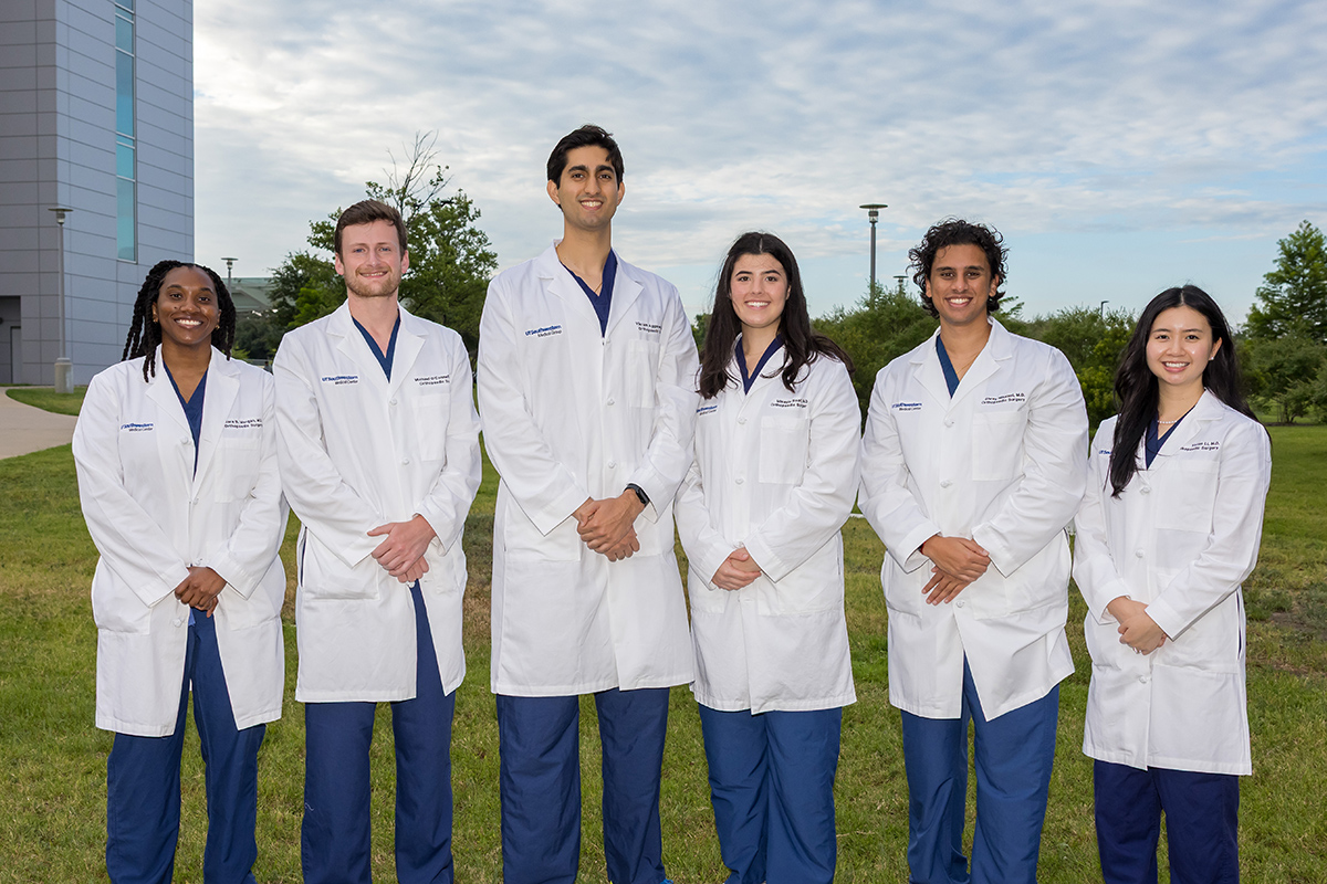  group of Orthopaedic Surgery Residents wearing white coats and blue scrubs standing outside hospital