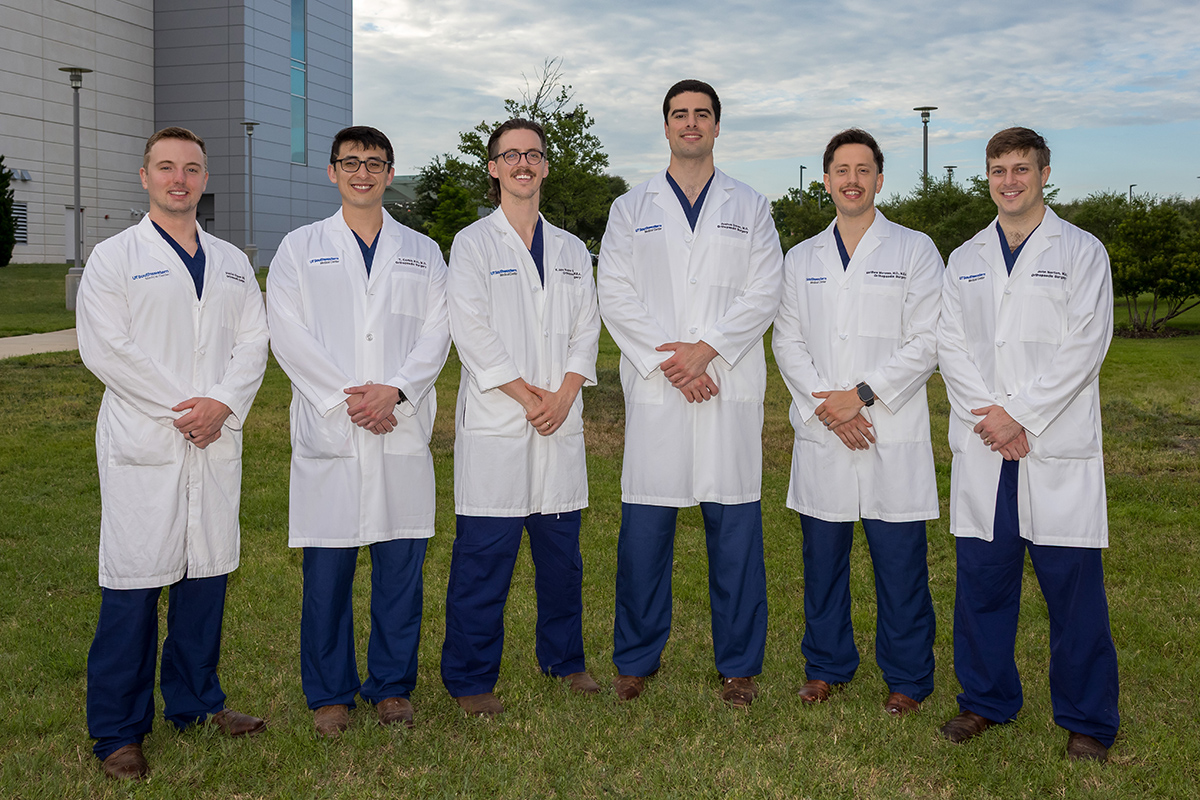 group of Orthopaedic Surgery Residents wearing white coats and blue scrubs standing outside hospital