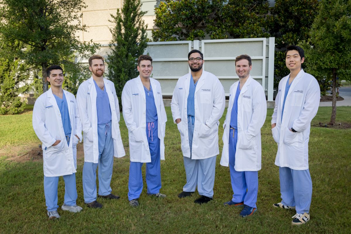 group of Orthopaedic Surgery Residents wearing white coats and blue scrubs standing outside hospital
