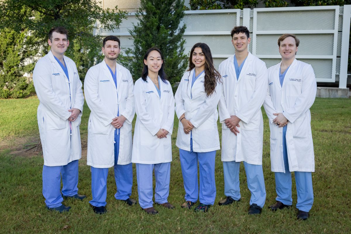 group of Orthopaedic Surgery Residents wearing white coats and blue scrubs standing outside hospital