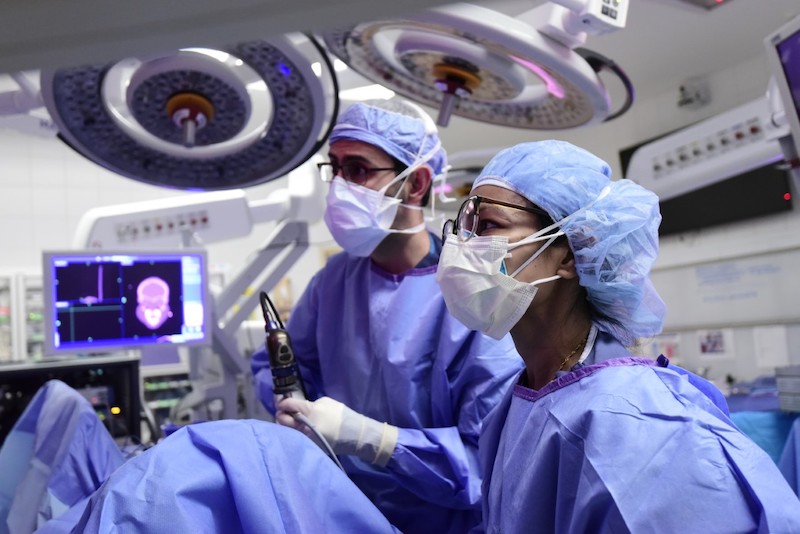 Two doctors in blue surgical gowns examining a patient