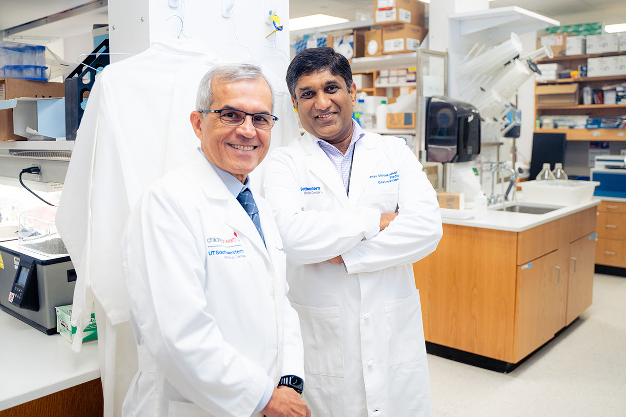 Two men in white coats standing in a lab and smiling at the camera
