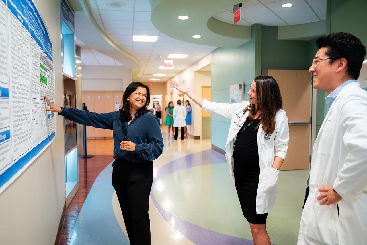 Two women and a man admire a poster in a hospital hallway