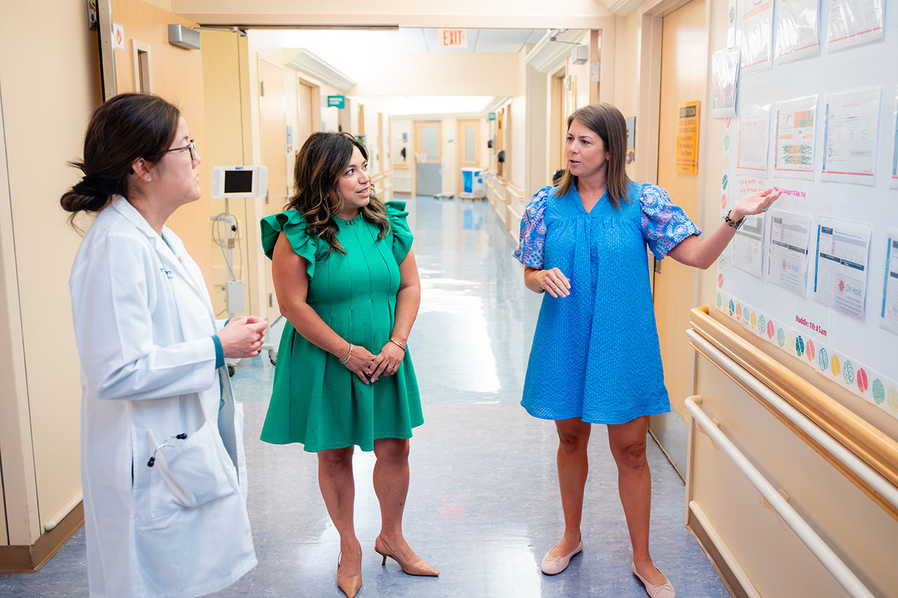 Three women discuss a bulletin board in a hospital hallway