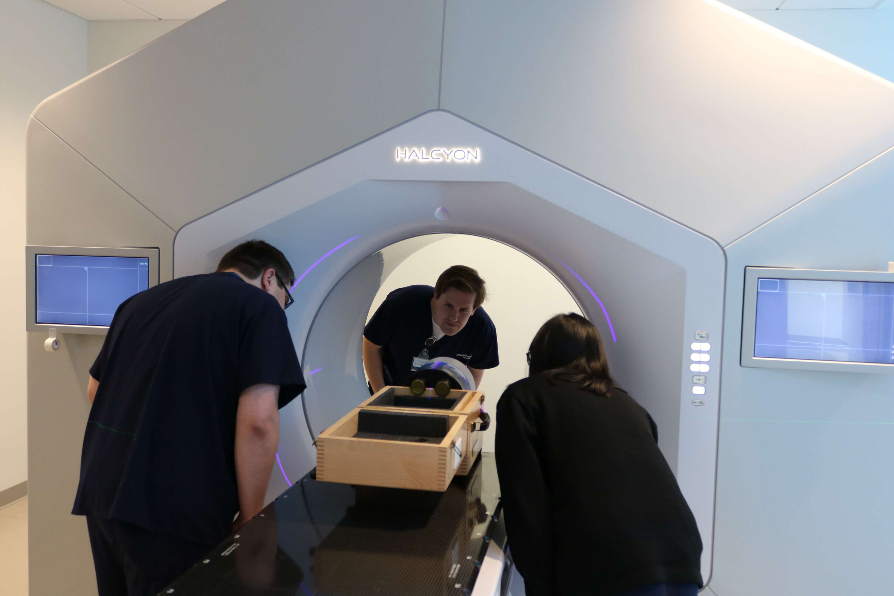 Three people in navy scrubs working at a radiation machine.
