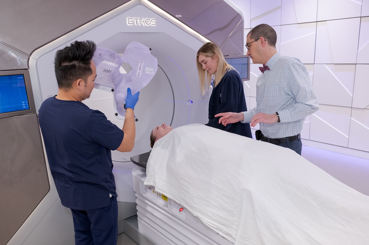 Three medical professionals prepare a patient lying on a table for a radiation therapy treatment using an ETHOS machine.