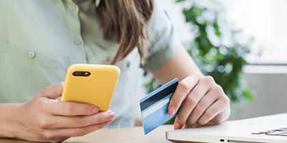 closeup of woman's hands holding cellphone with yellow case and a credit card in front of a laptop