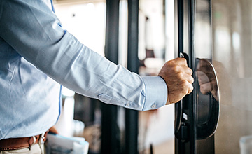man's arm in dress shirt, hand grasping metal handle on glass door