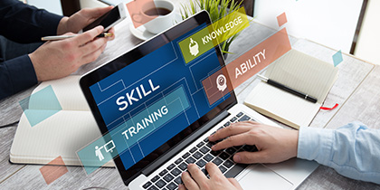 man's hand and sleeve on laptop keyboard with display showing abstract graphic with text SKILL TRAINING ABILITY and open notebook with pen to right side