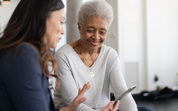 woman with dark hair shows phone to older grey haired woman in white sweater