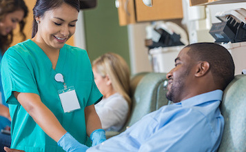 nurse in green scrubs touches arm of male patient in chair
