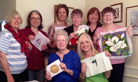 group of 8 women hold up needlework creations. 