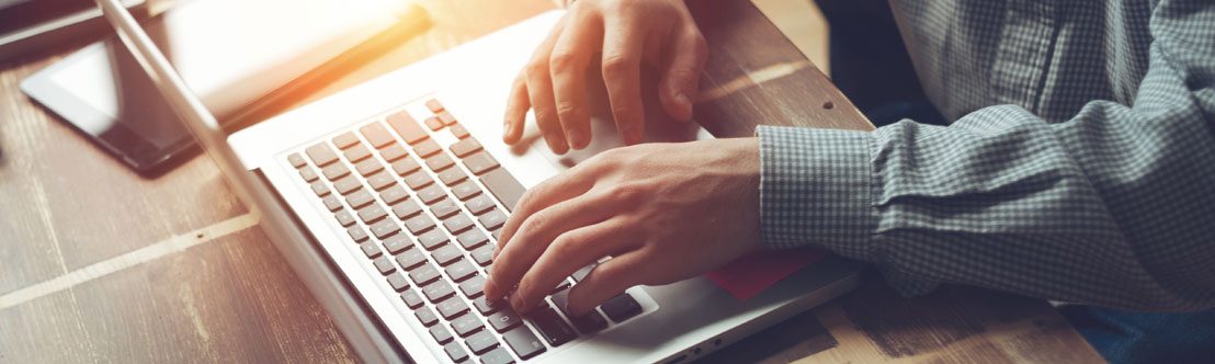A close-up photo of a man's hands typing on a laptop computer