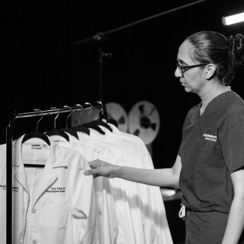 Dr. Patel viewing a row of white coats, hanging up on a rack.