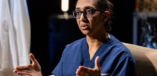 Dr. Patel wearing her bue scrubs, talking in an interview.