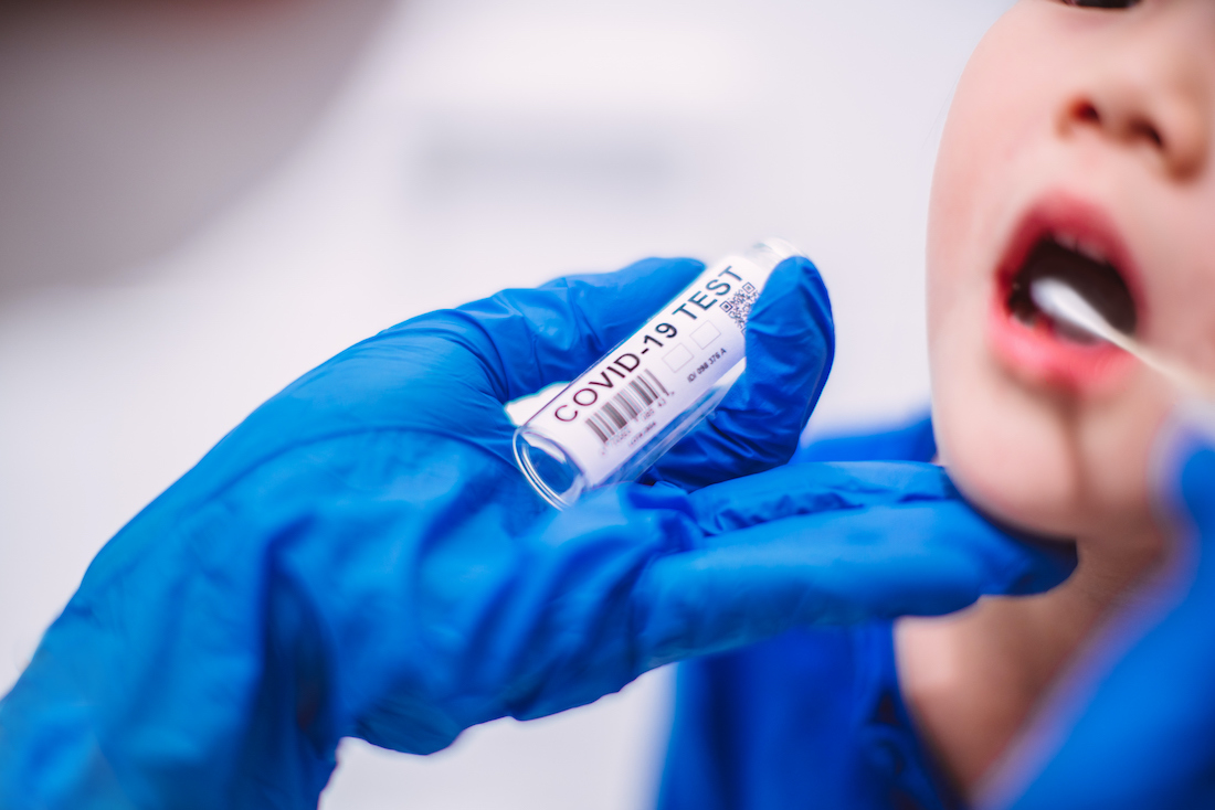 Doctor&rsquo;s hands in protection gloves putting COVID-19 test swab into kid&rsquo;s mouth in hospital.