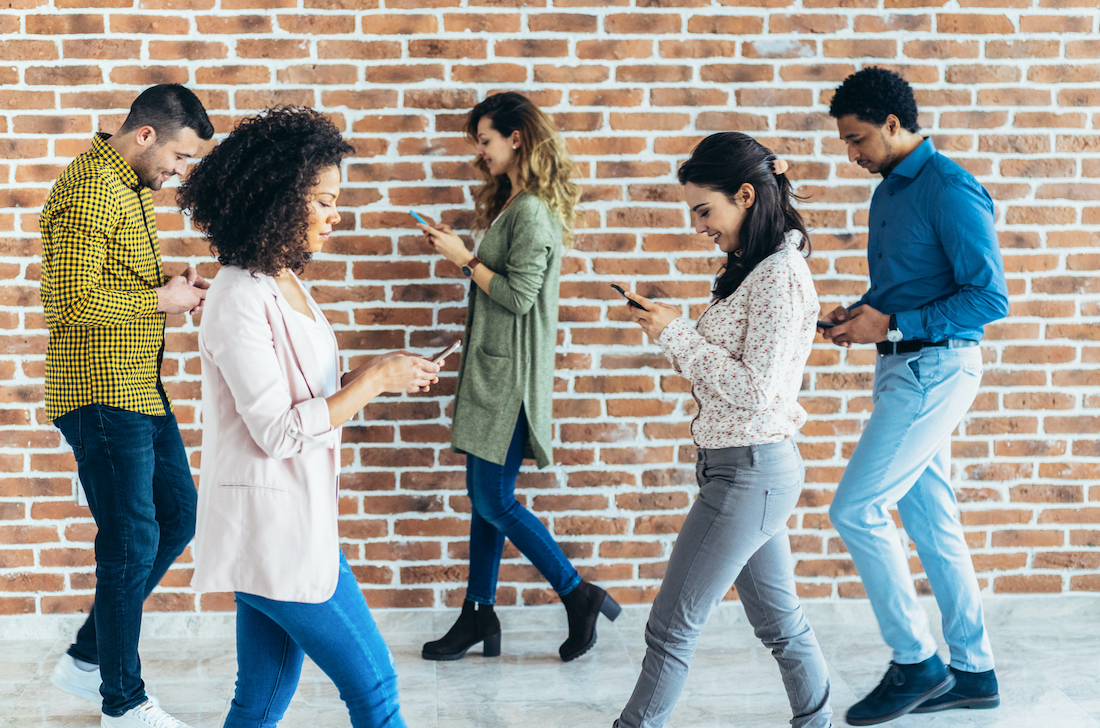 Young people using digital devices waking on the street with brick wall behind
