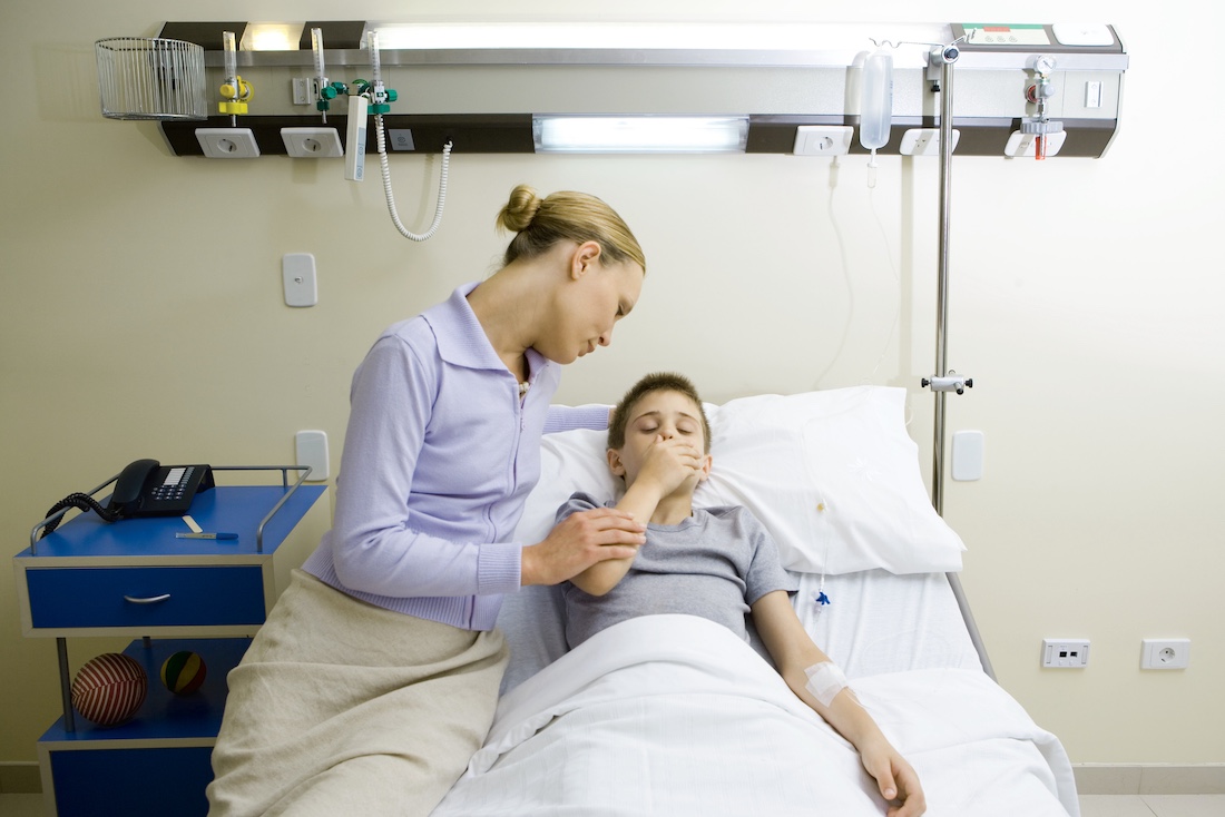Boy lying in hospital bed, mother sitting by side