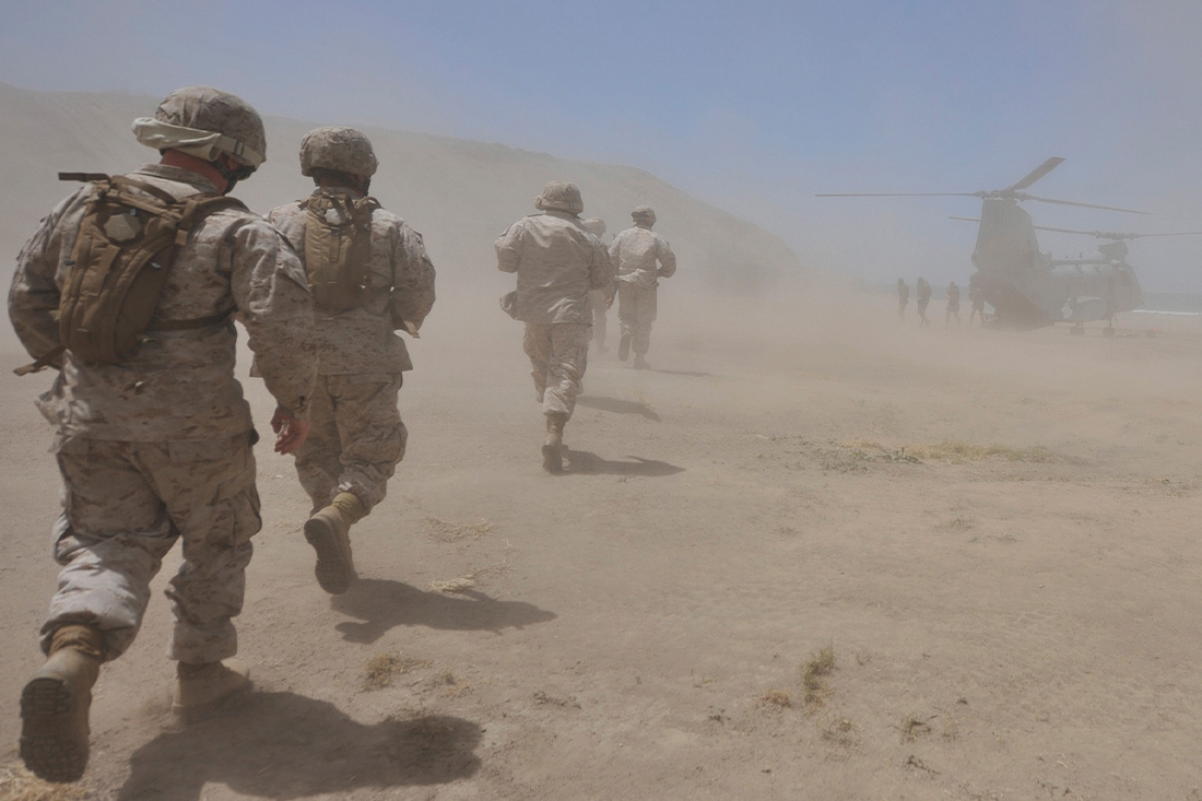 Marines move through a dust cloud toward a CH-46 Sea Knight.