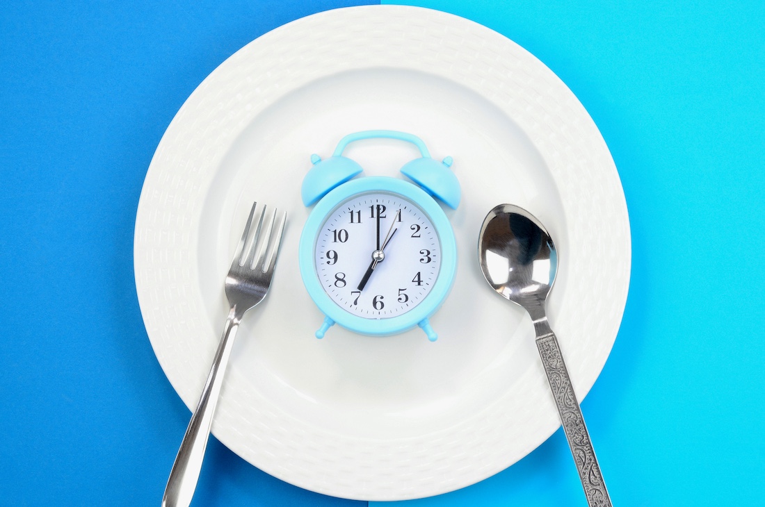  Concept of diet and weight loss. Alarm clock on a white plate.
