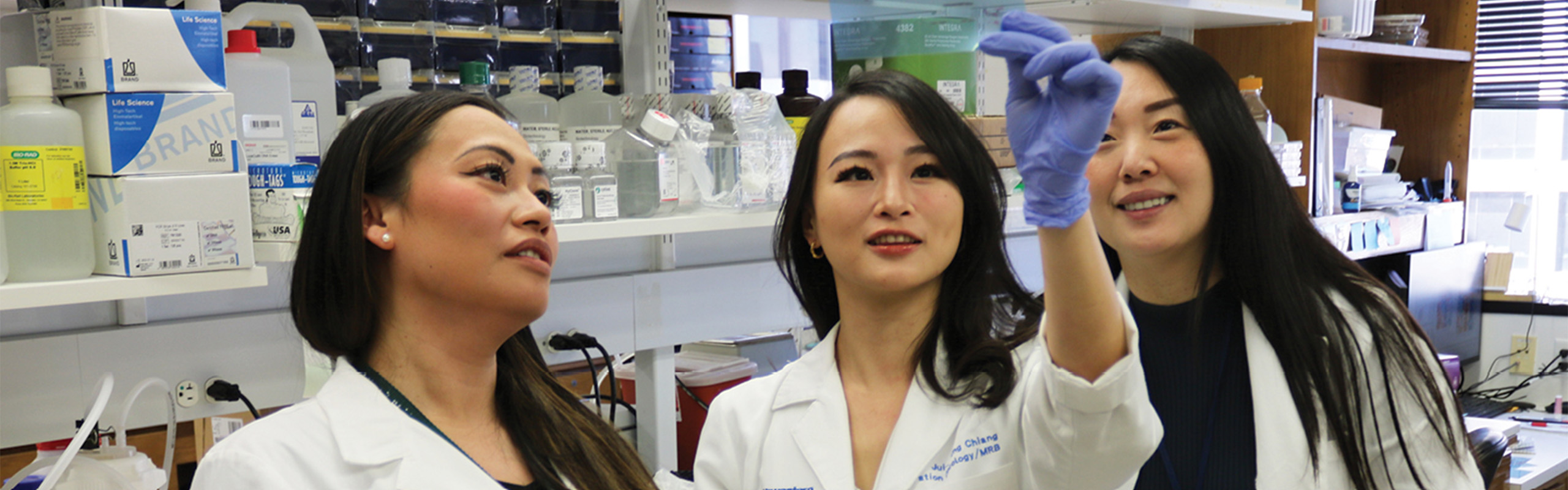 Three women in lab coats examine a sample